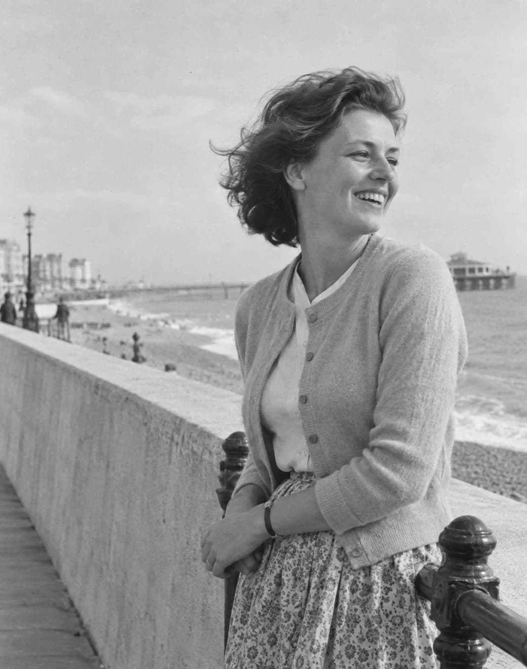 Illustrated family-album scene of a woman laughing on Brighton promenade in 1963.